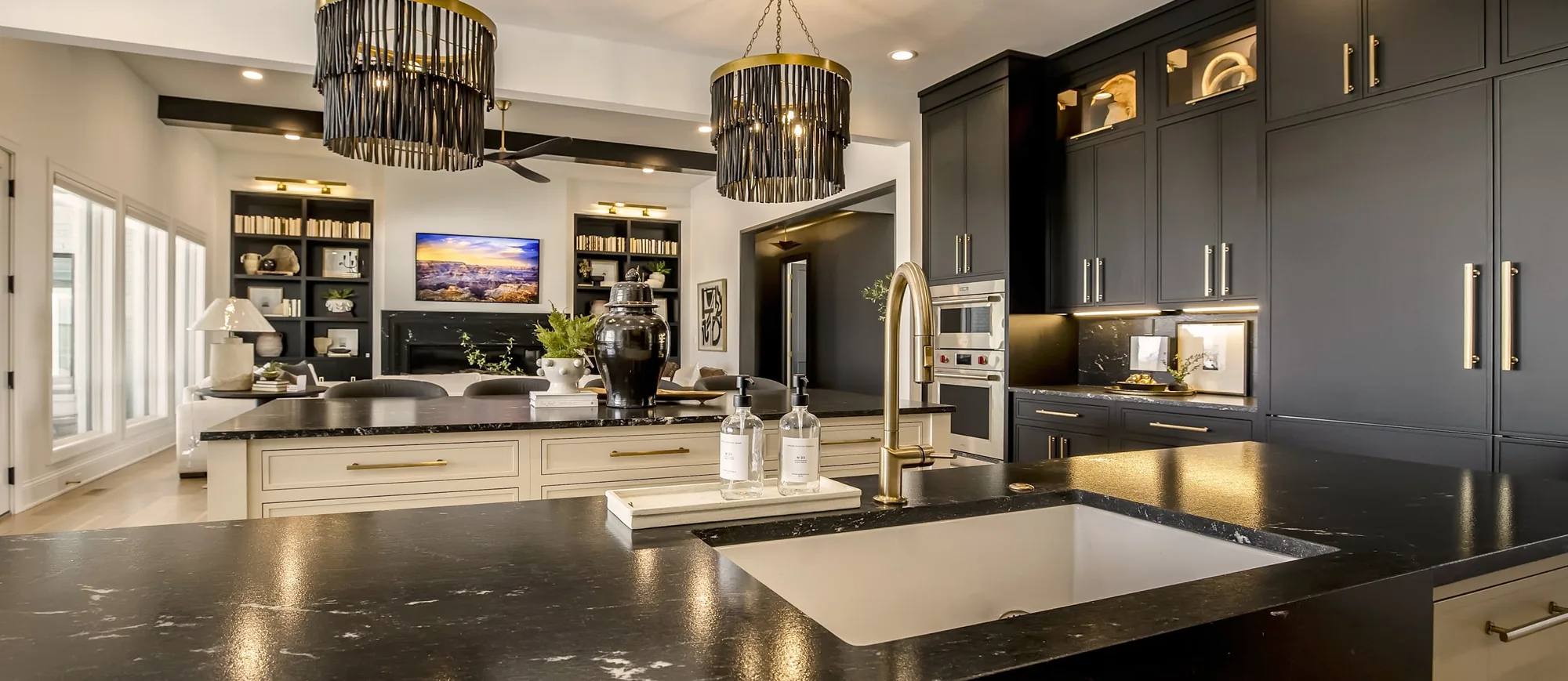 Kitchen with charcoal cabinetry, a dark veined stone island and brass fittings, open to a living room