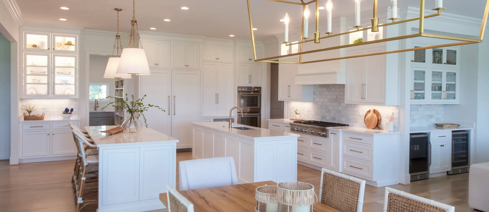 A wide, light kitchen with two islands, glass-front upper cabinetry and a brass lantern over the dining table