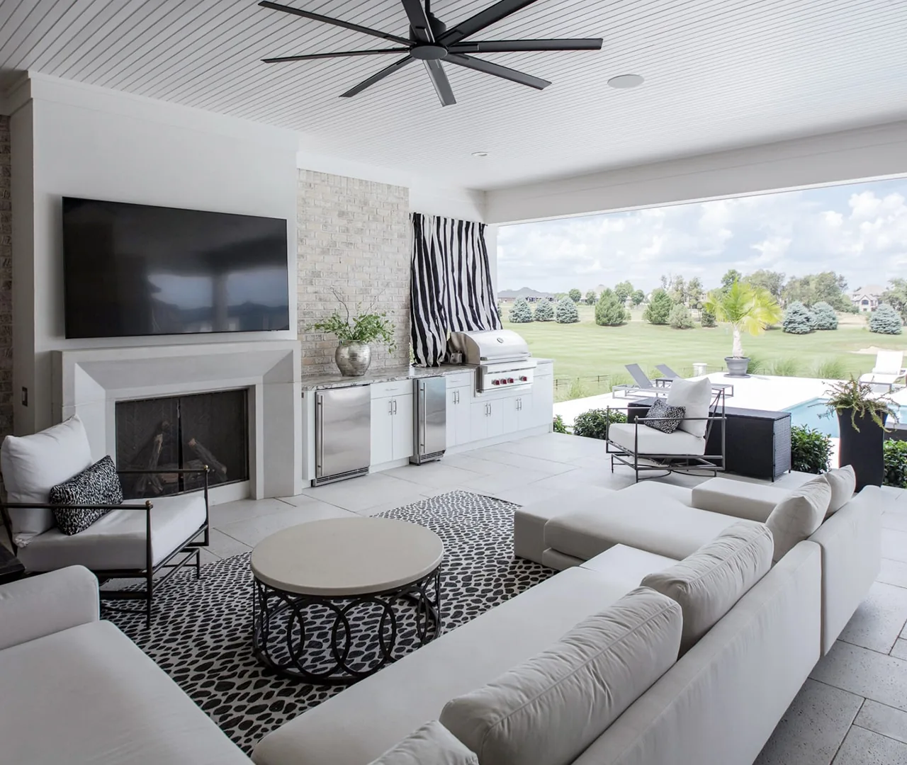 Covered outdoor living space with a grill run, fireplace and open view to a lawn