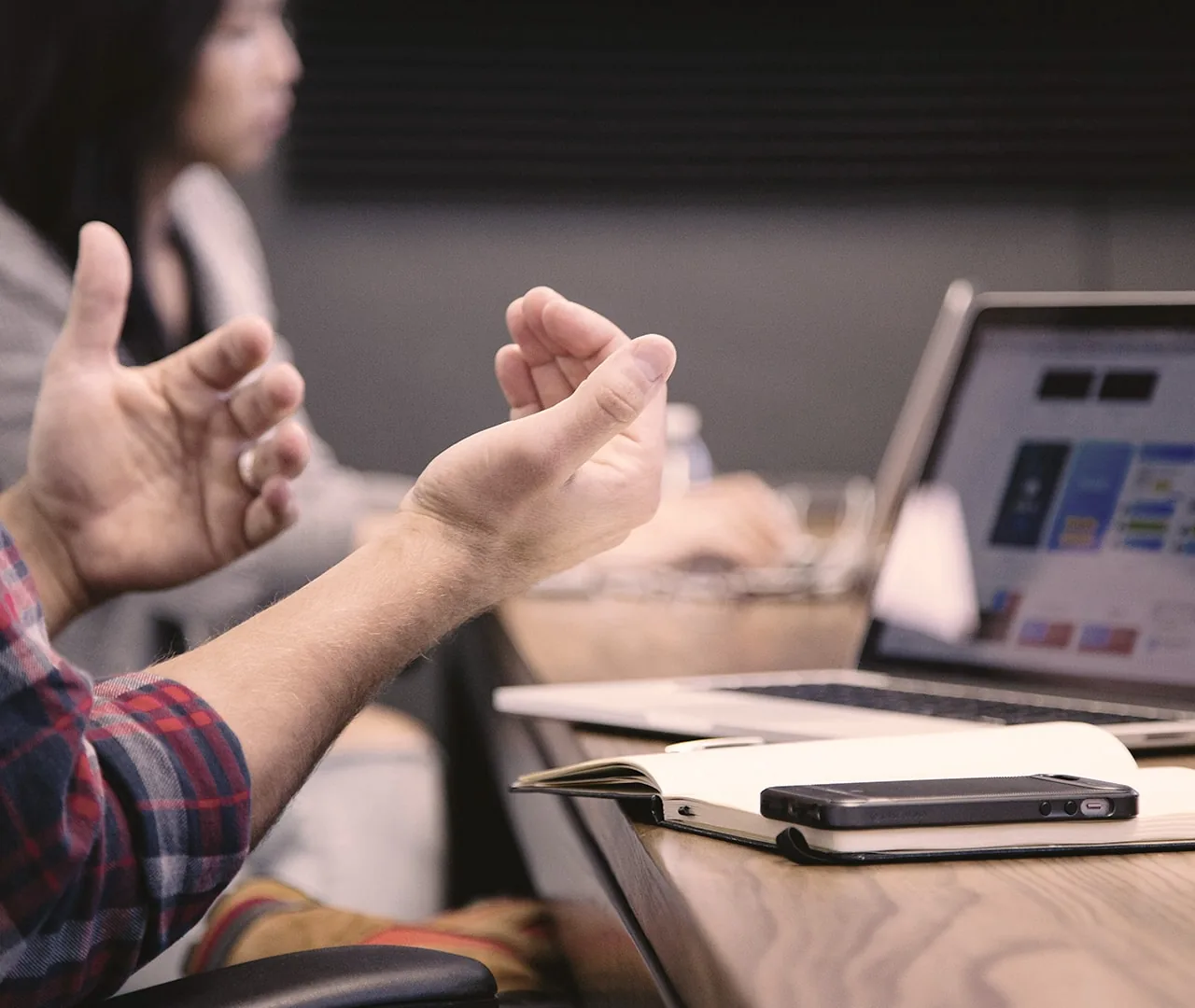 Two people talking across a table with a laptop open between them