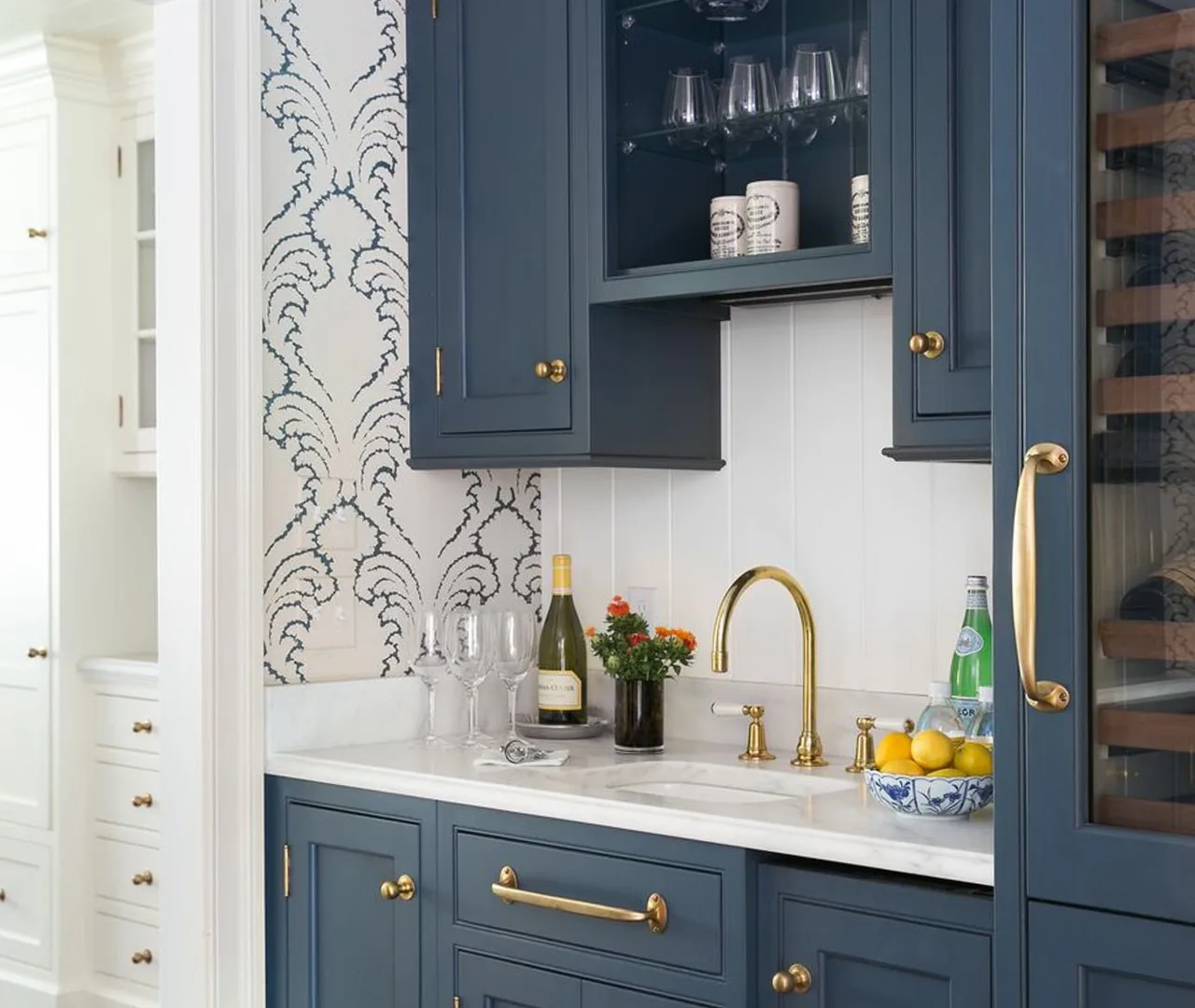 Wet bar with navy cabinetry, glass uppers, brass fittings and a patterned backsplash